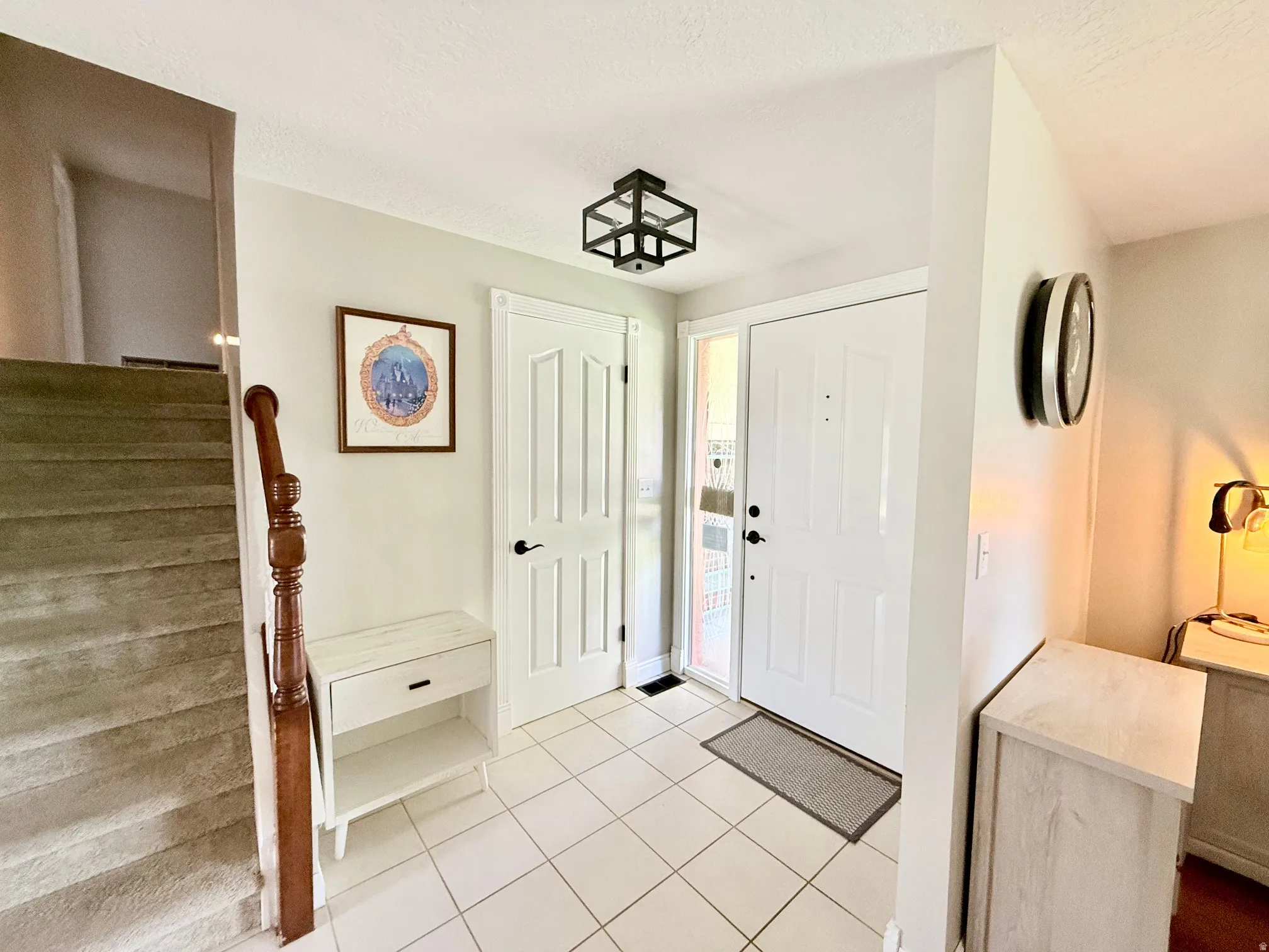 White paneled door with sidelight, tile flooring, and staircase with wood banister