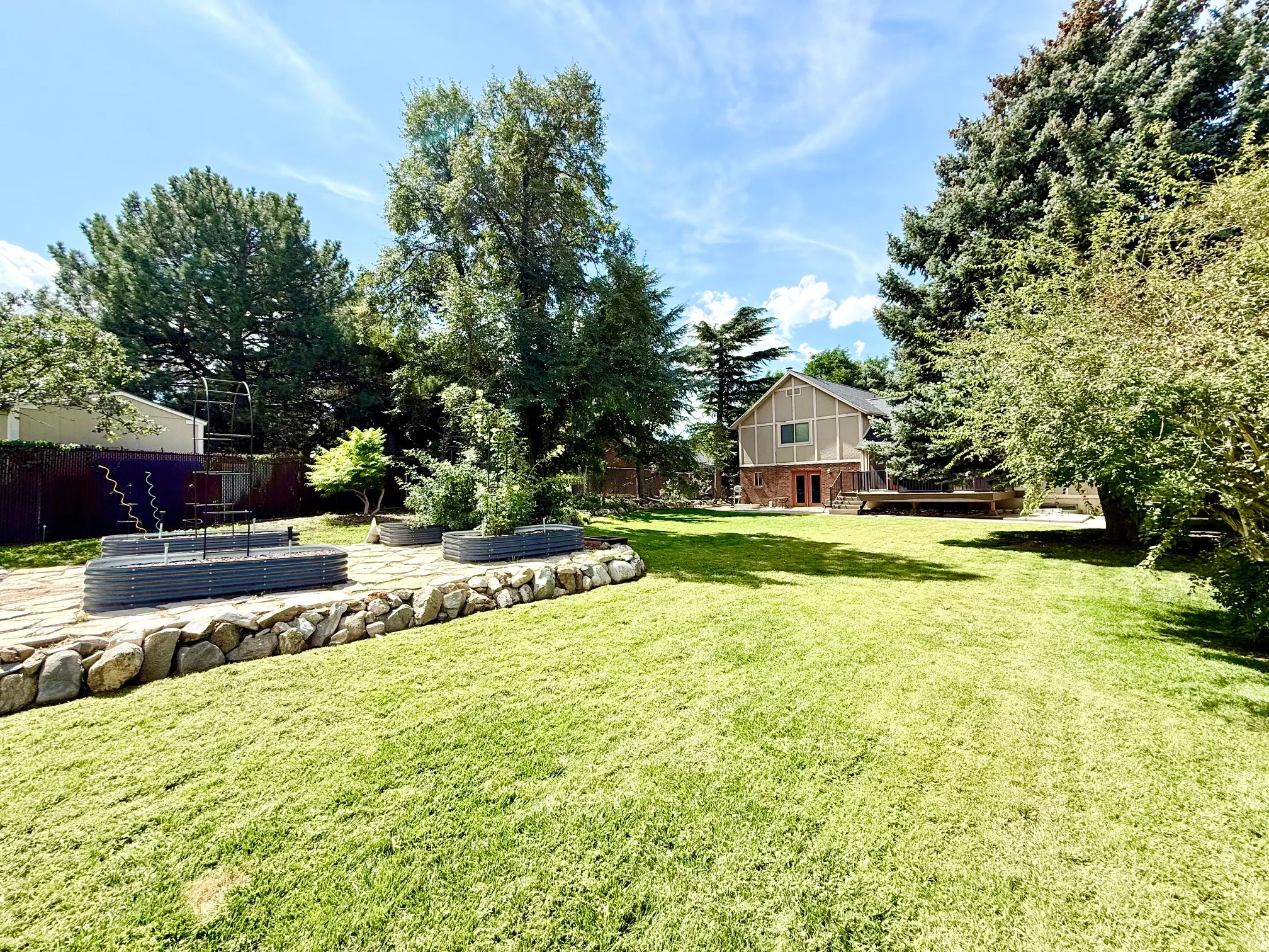 Expansive green lawn with a rock retaining wall and raised garden beds