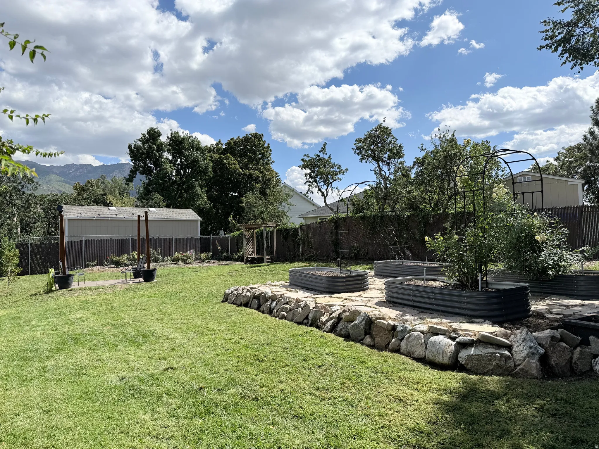 Expansive lawn featuring multiple raised garden beds, a stone retaining wall, and mountain scenery in the background