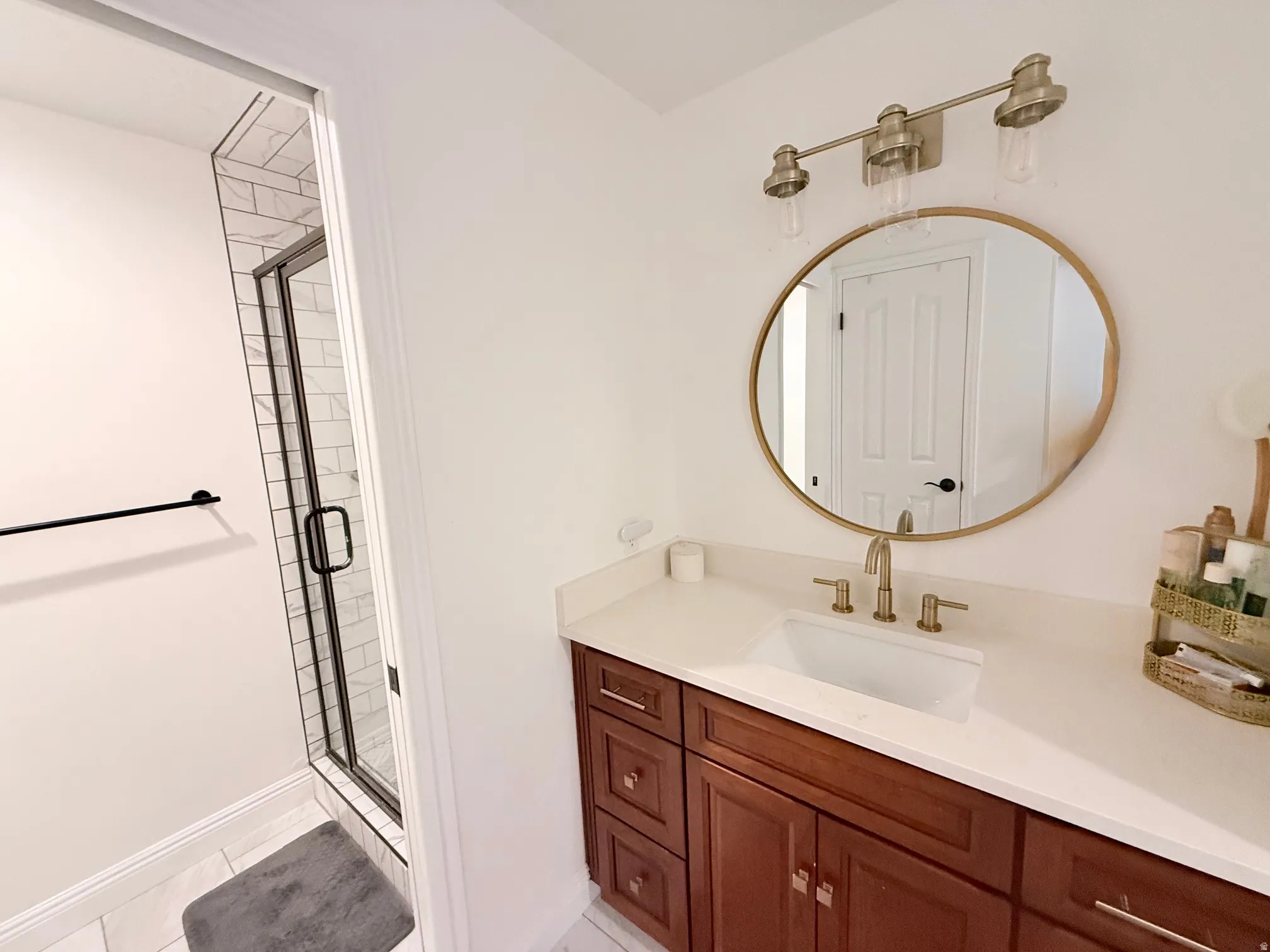 White subway tile shower with black-framed glass enclosure, wood-finish vanity with countertop, rectangular undermount sink, and a round wall-mounted mirror