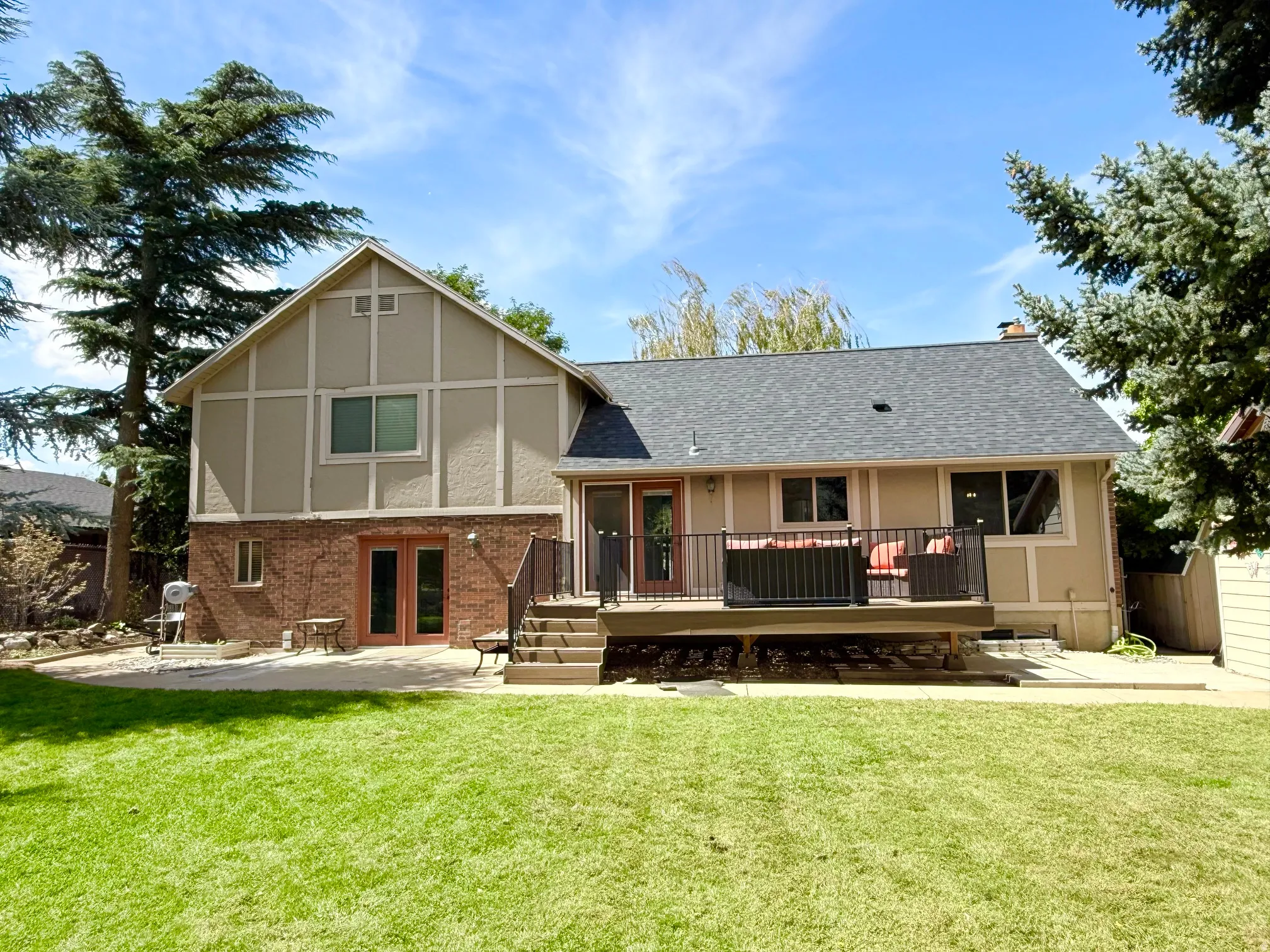 Expansive green lawn with a large rear deck featuring metal railings, and a lower-level patio