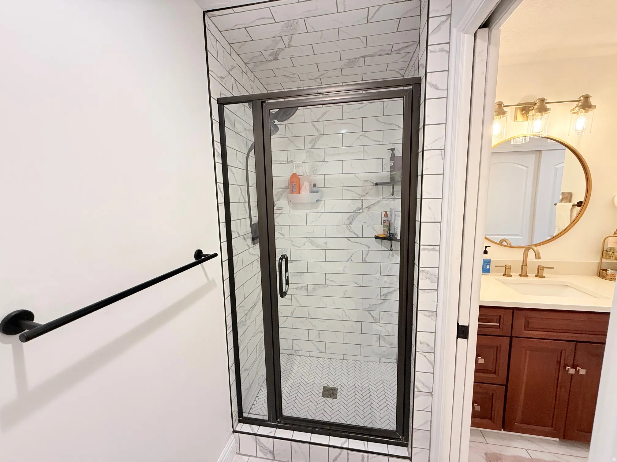 Glass-enclosed shower with white subway tile surround, herringbone pattern shower floor, and matte black fixtures