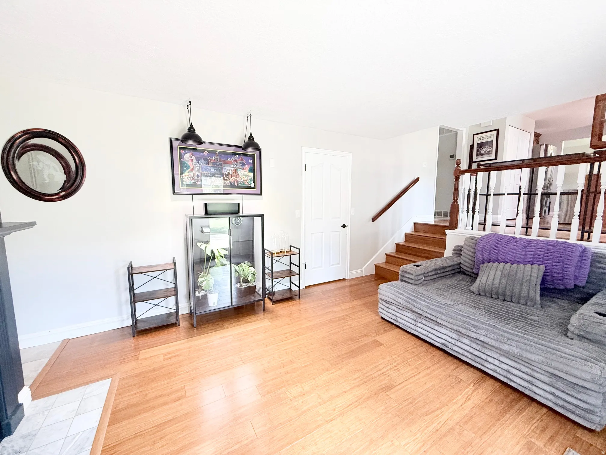 Hardwood flooring, painted white walls, wood staircase with white balusters, white paneled door, and built-in shelving