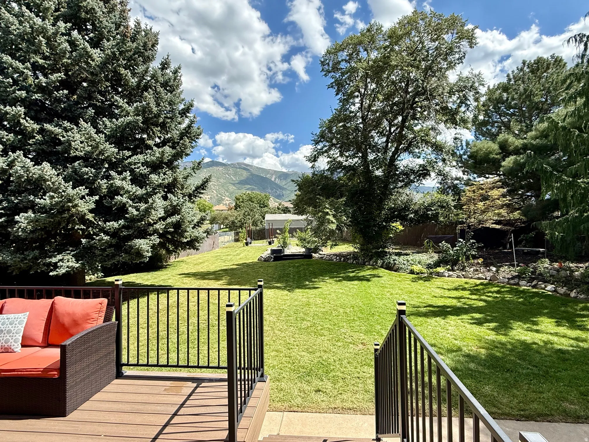 Expansive backyard featuring a green lawn, mature trees, and a multi-level deck with black railings