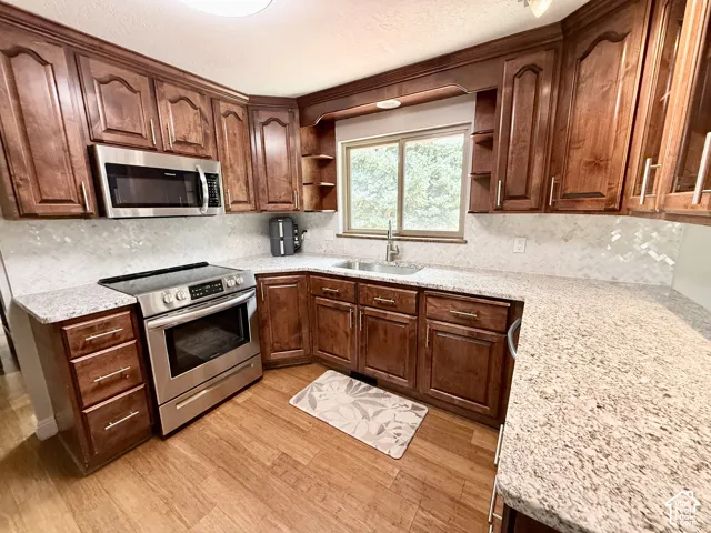 Warm wood cabinetry with brushed nickel hardware, stainless steel appliances, granite countertops, and a full-height tile backsplash