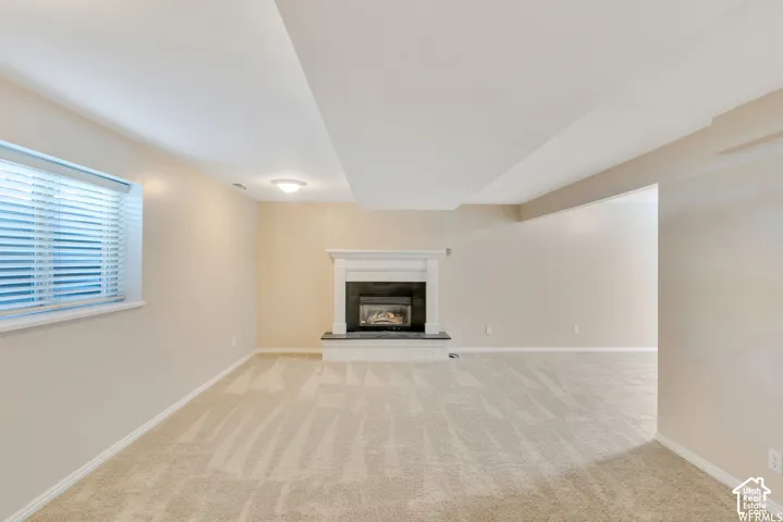 Integrated fireplace with white mantel and dark surround, plush carpet flooring, recessed lighting, and a window with blinds