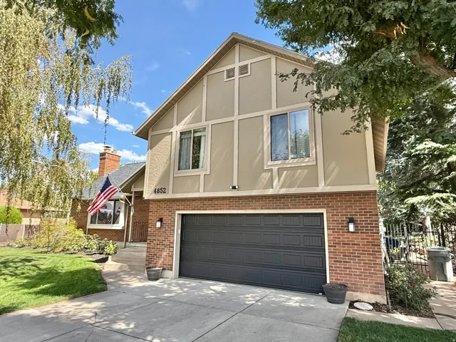 Brick and stucco exterior with dark garage door, concrete driveway, and established landscaping