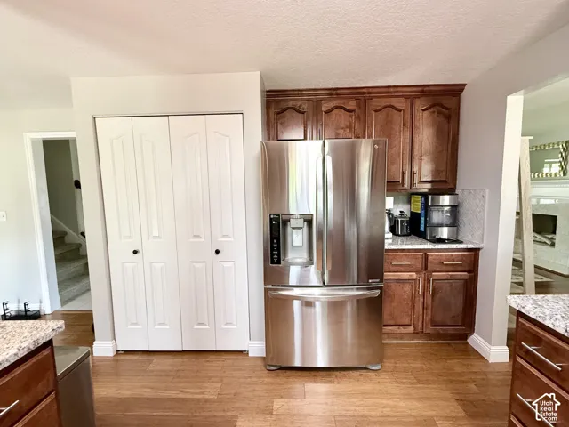 Wood-finish flooring, cherry-toned cabinetry, stainless steel refrigerator, granite-look countertops, and white bifold doors