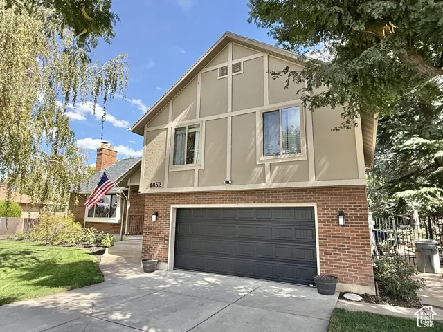 Brick and stucco exterior with dark garage door, concrete driveway, and established landscaping