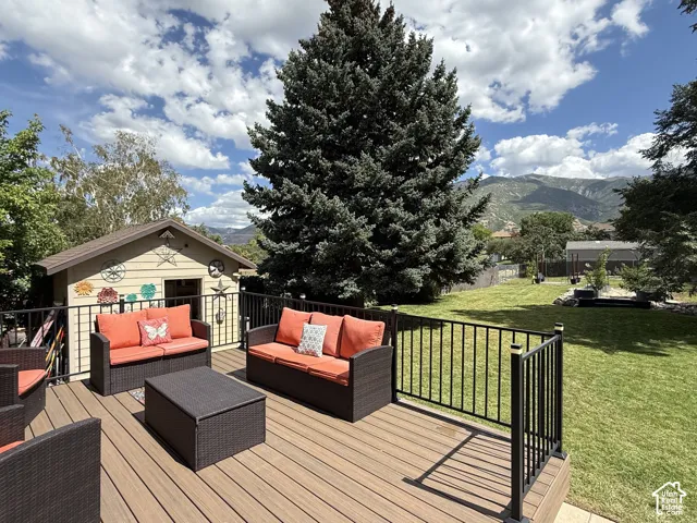 Expansive wood-finish deck with black metal railings, overlooking a large grassy yard with mature trees
