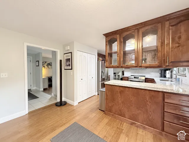 Kitchen featuring stained wood cabinetry with glass-front uppers, stone countertops, stainless steel appliances, and wood-finish flooring