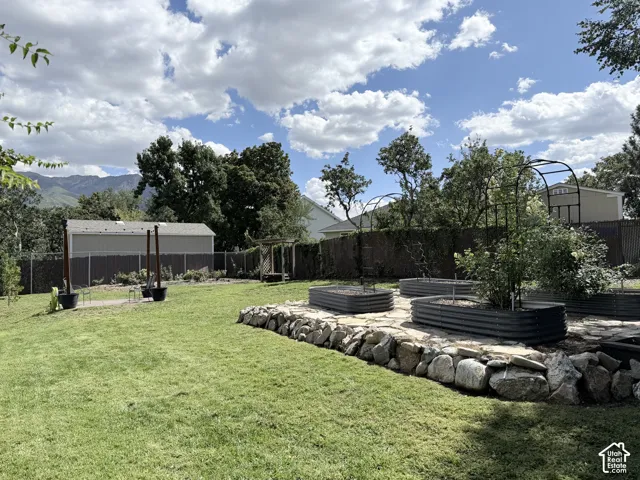 Expansive lawn featuring multiple raised garden beds, a stone retaining wall, and mountain scenery in the background