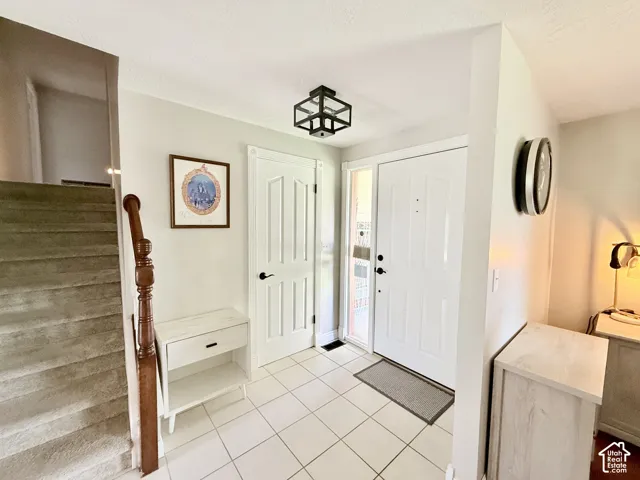 White paneled door with sidelight, tile flooring, and staircase with wood banister