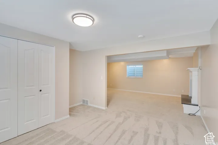 Neutral tone wall paint, light-colored carpeting, white bi-fold closet doors, white mantel with dark hearth, and a single window with blinds