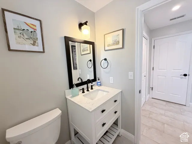 Vanity with a white countertop and integrated sink, black-framed mirror, contemporary wall sconce, and wood-finish tile flooring