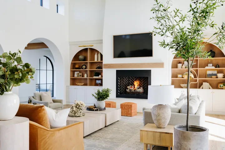 Vaulted ceilings with arched architectural details, fireplace with wood mantel, built-in shelving with lower cabinetry, and dark-framed arched doorway