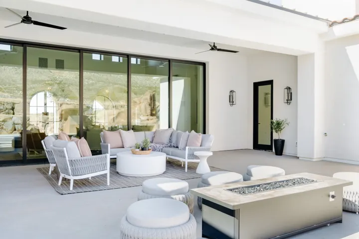 Expansive covered patio featuring sliding glass doors, dual ceiling fans, a gas fire pit, and wall-mounted sconces
