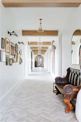 Elongated hallway featuring wood-finish ceiling beams, arched entries, and a series of globe pendant lights