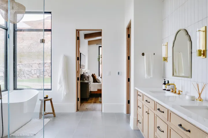 Freestanding soaking tub, floor-to-ceiling windows, dual vanity with wood-finish cabinetry, tile flooring, and vertical subway tile accent wall