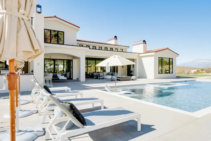 Expansive pool deck with integrated pool and spa, featuring a stucco exterior with a tile roof, an outdoor kitchen, and large sliding glass doors