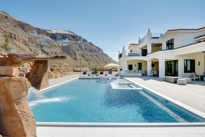 Expansive outdoor living area featuring a large swimming pool, integrated spa, and rock waterfall feature
