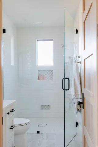 Glass-enclosed shower with subway tile walls, dual recessed niches, and a small window