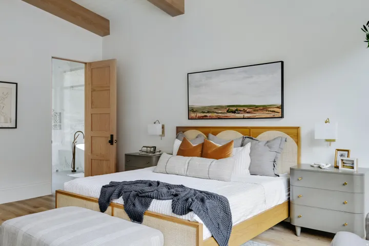 Vaulted ceiling with exposed wood beams, wood-finish flooring, solid wood panel door, recessed wall lighting, and a freestanding soaking tub