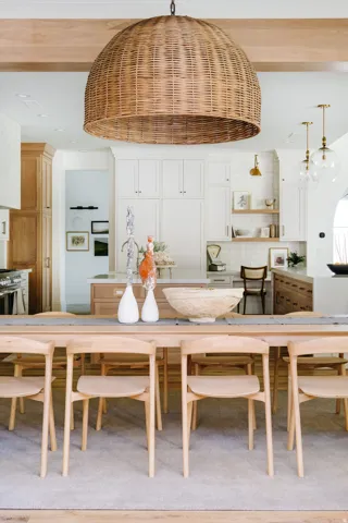 Woven pendant light fixture, exposed wood ceiling beam, light wood-finish flooring, white cabinetry, and a large central island