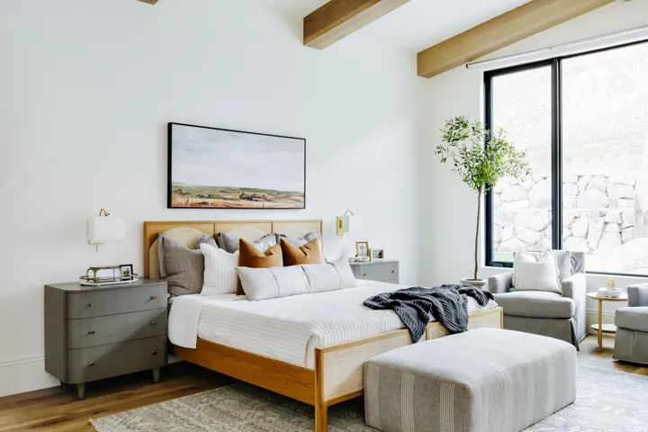 Vaulted ceiling with exposed wood beams, large format window, wall-mounted light fixtures, wood-finish flooring, and built-in wall sconces