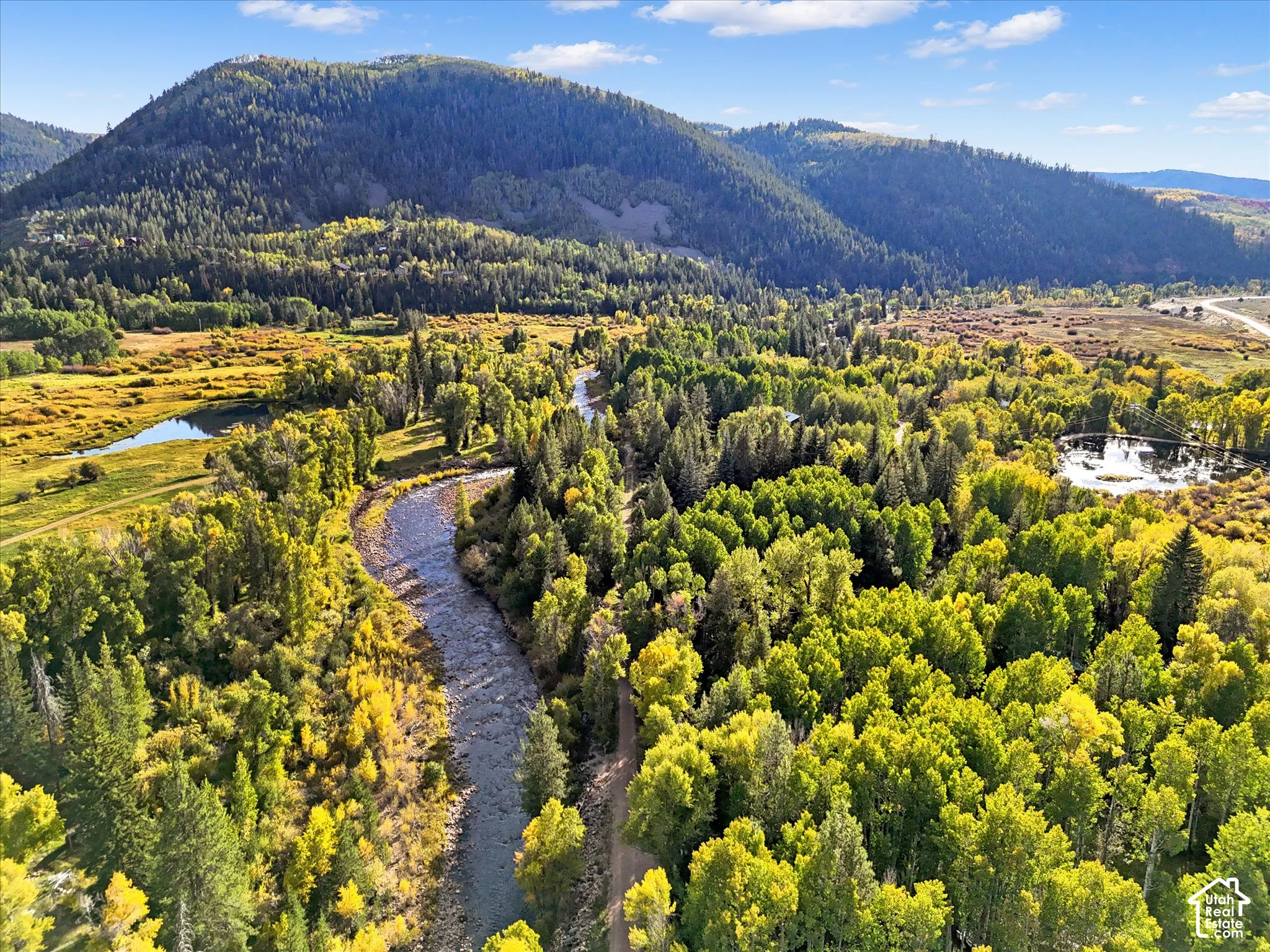 Expansive natural landscape featuring a winding river, dense deciduous and evergreen trees, a distant mountain range, and scattered bodies of water