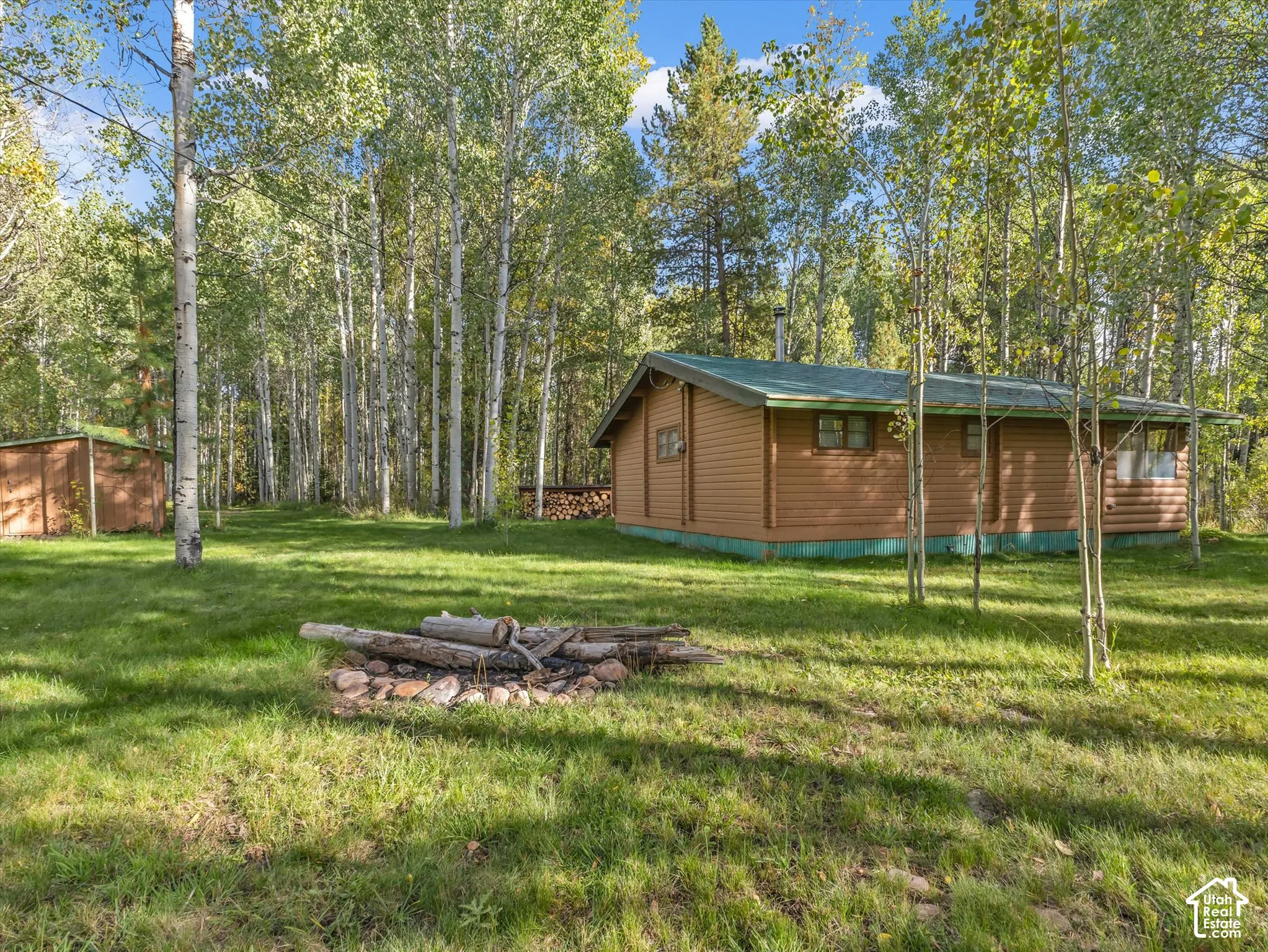 Wood-sided cabin with a green roof, surrounded by mature trees