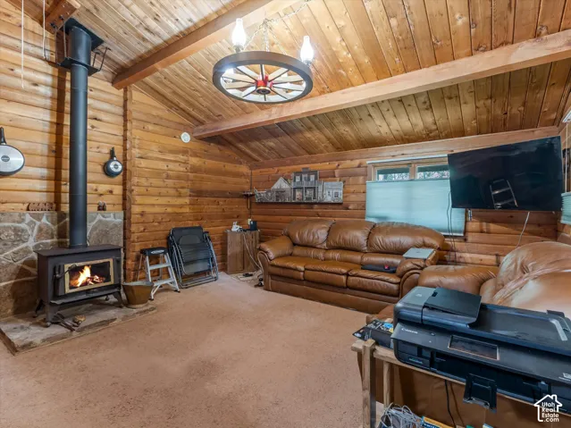 Wood-paneled walls and ceiling with exposed beams, wood-burning stove with stone surround, wagon wheel chandelier, and window with privacy blinds