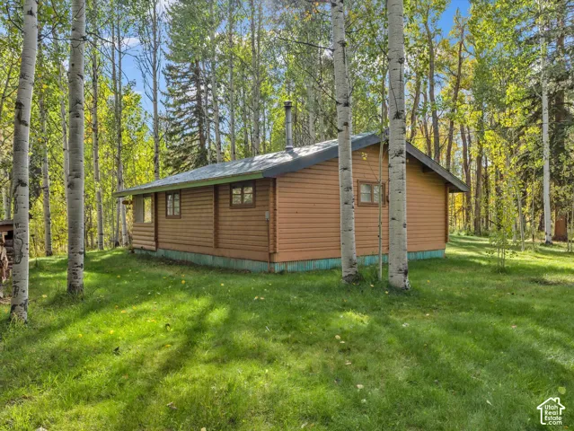 Wood-sided cabin featuring multiple windows, a dark roof, and a chimney