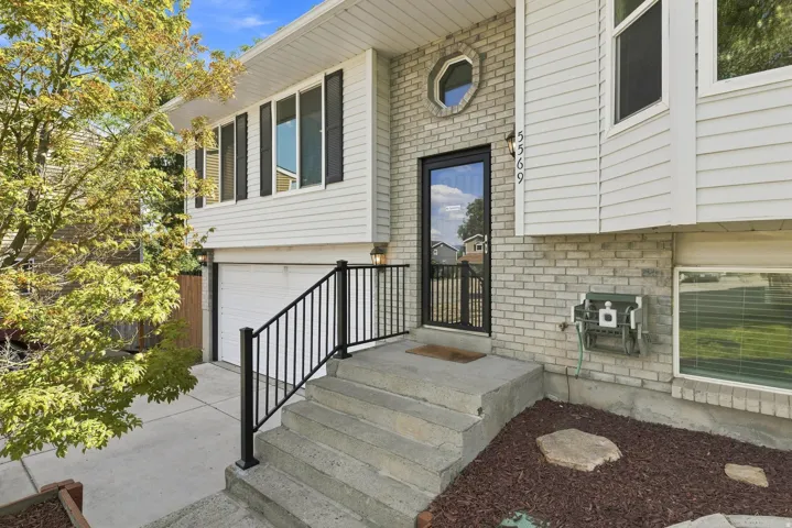 Exterior featuring white siding, a brick facade, an attached garage, a contemporary entry door with a decorative screen, and a paved driveway