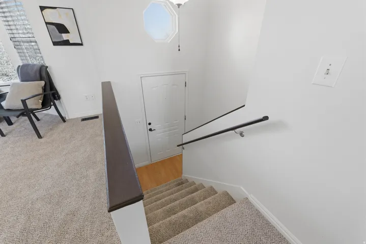 Carpeted stairs with a dark wood-finish railing, white walls, and an octagonal ceiling light fixture