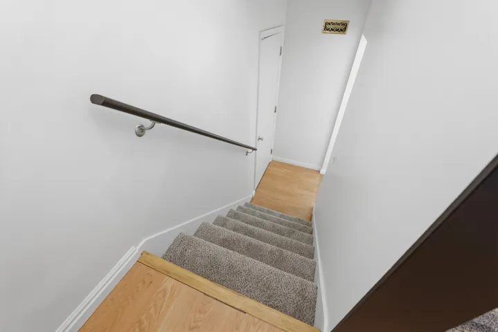 Carpeted staircase with wood-finish treads and a dark-toned handrail
