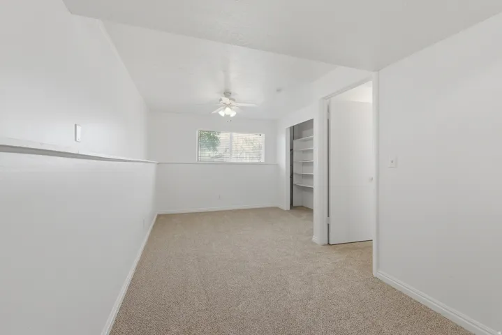 Neutral-toned carpeting, white walls, built-in closet shelving, and a ceiling fan with integrated lighting