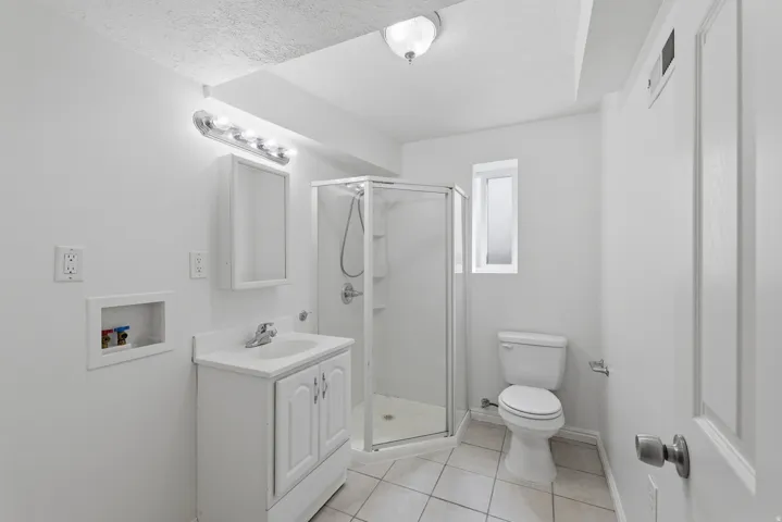 White vanity with integrated sink, glass-enclosed shower, built-in medicine cabinet, and tile flooring