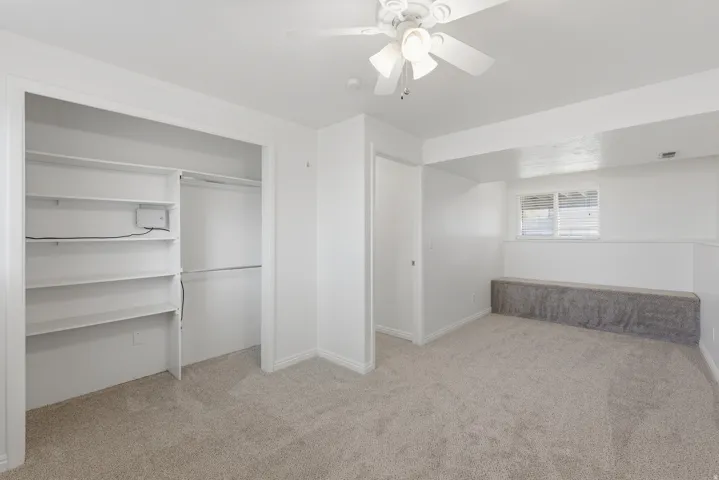 Recessed window, built-in storage shelving, ceiling fan, neutral carpet, and white walls