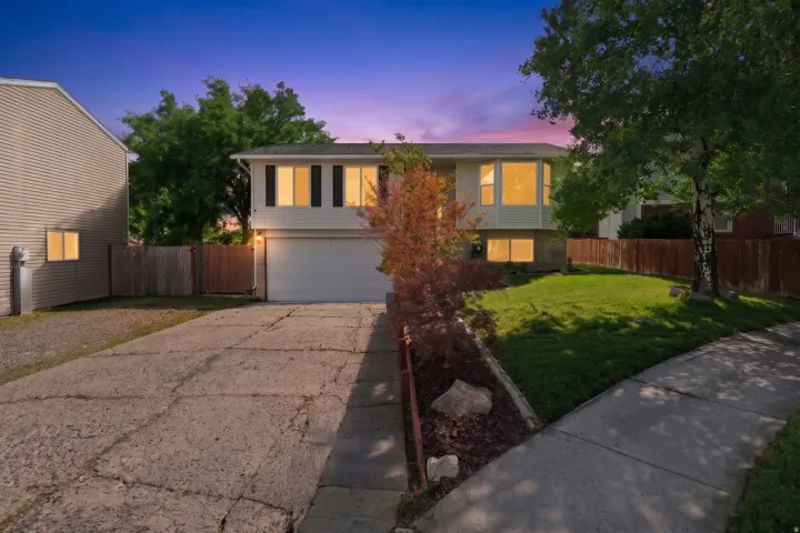 Split-level residence featuring a two-car garage, front lawn, and mature trees