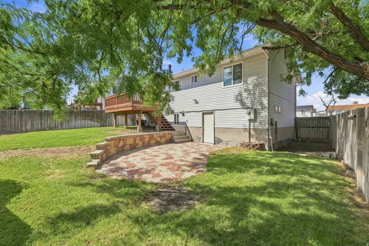 Expansive backyard featuring a manicured lawn, a two-story deck with wood railings, a stone patio, and privacy fencing