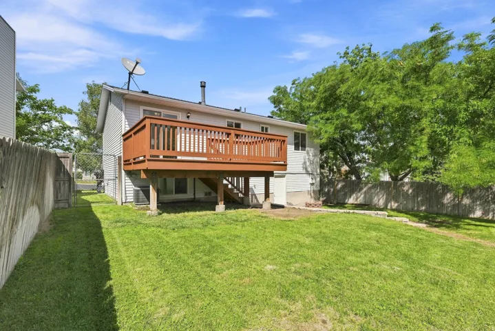 Expansive grassy backyard featuring a large elevated wood deck, mature trees, and privacy fencing