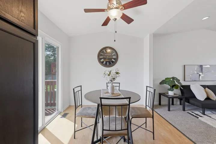 Vaulted ceiling with an attached ceiling fan, wood-finish flooring, white walls, and a sliding glass door leading to a wooden deck