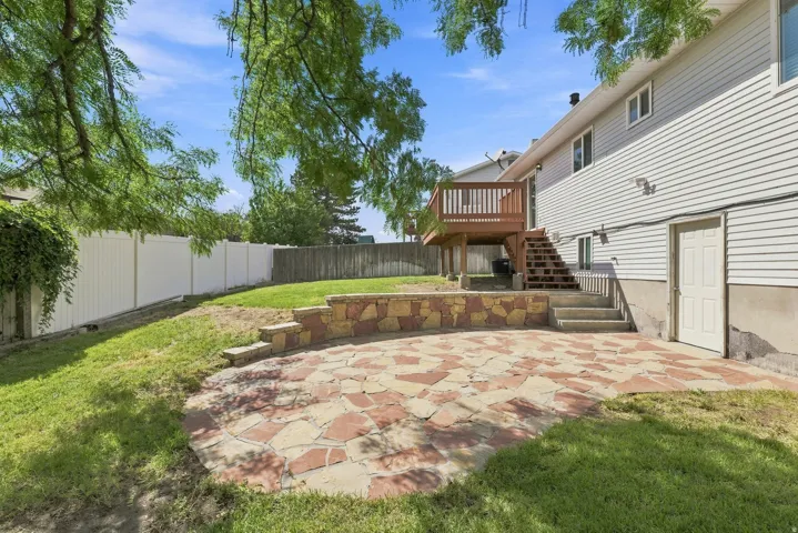 Expansive backyard featuring a stone patio, stone retaining wall, and a raised wood deck with stairs