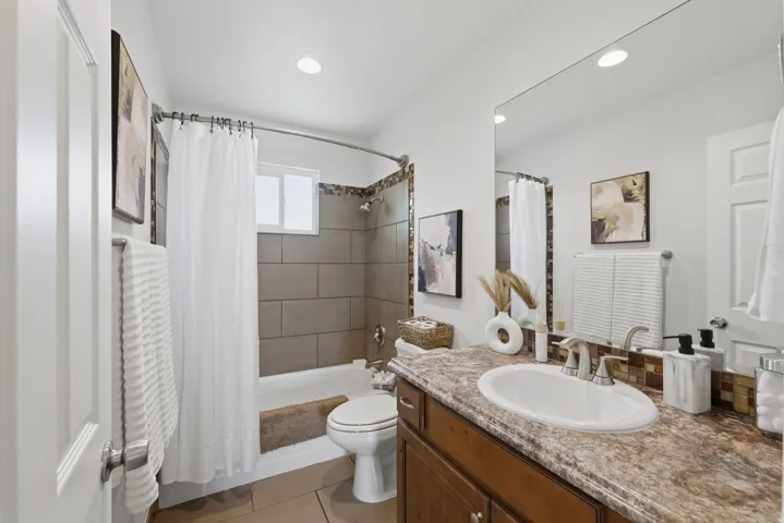 Vanity with an oval undermount sink, wood-finish cabinetry, and a full-width mirror
