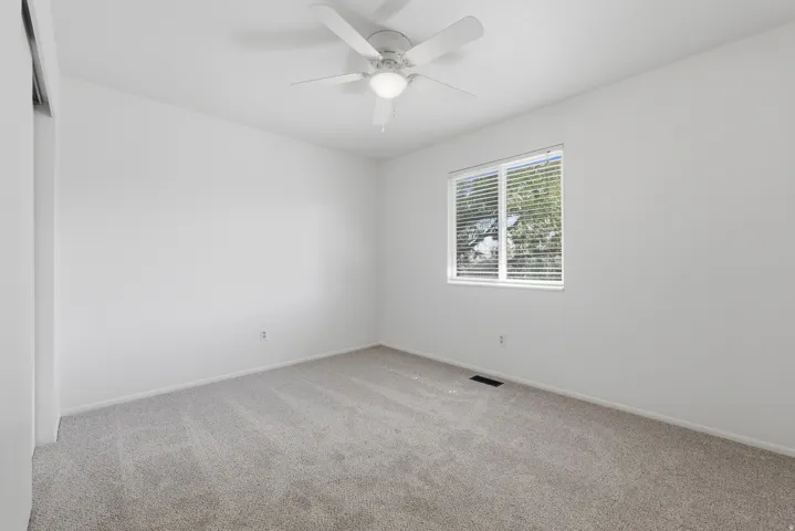 Carpeted room with a single window, white window blinds, and a ceiling fan with integrated lighting