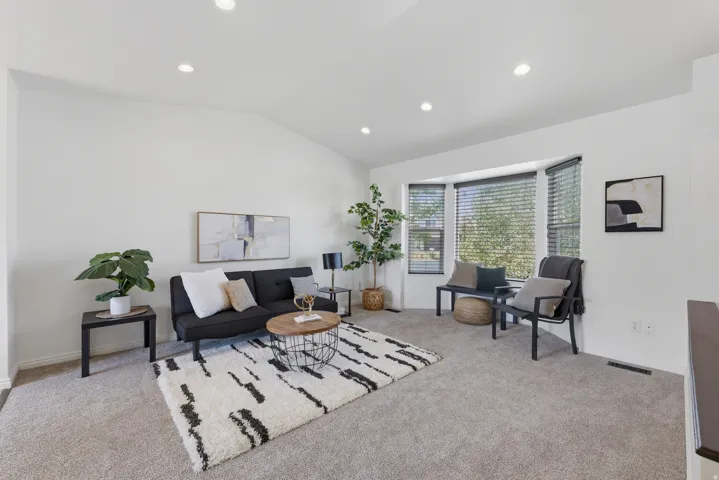 Vaulted ceilings with recessed lighting, bay windows with blinds, and light-toned carpeting