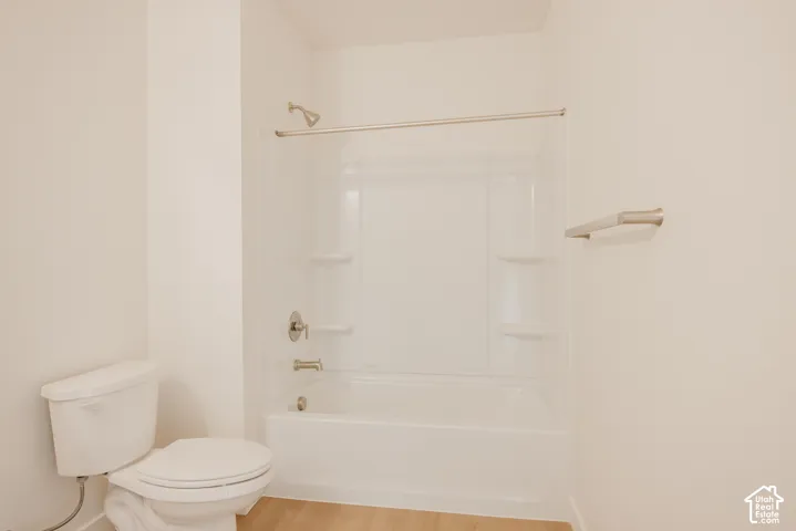 Tub and shower combination with a curved shower curtain rod, white toilet, and light wood-finish flooring