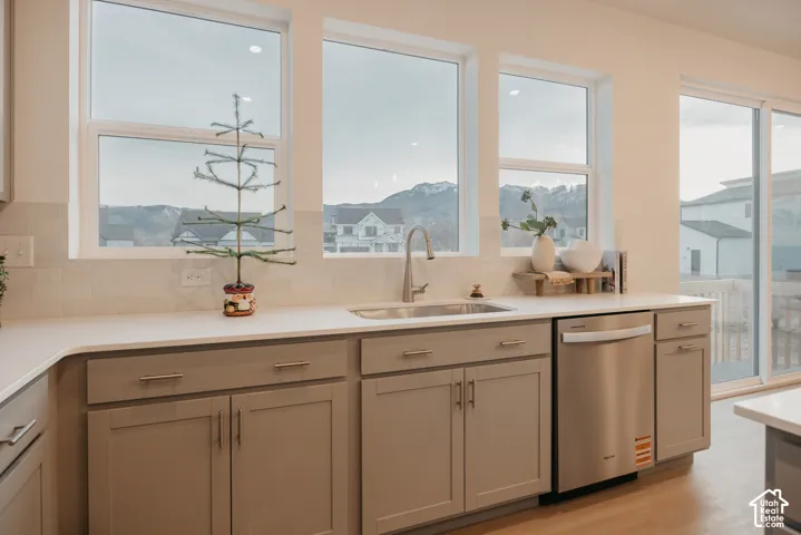 White countertops, undermount stainless steel sink, stainless steel dishwasher, and light gray cabinetry