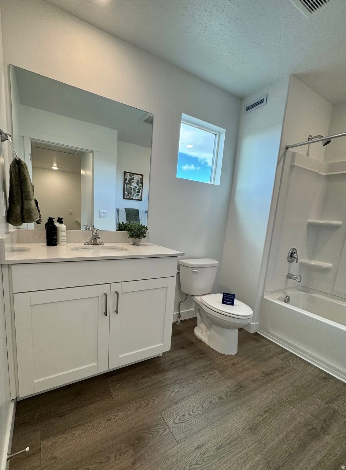 White shaker-style vanity with a light-toned countertop, wood-finish flooring, a white toilet, and a white shower-over-tub combination